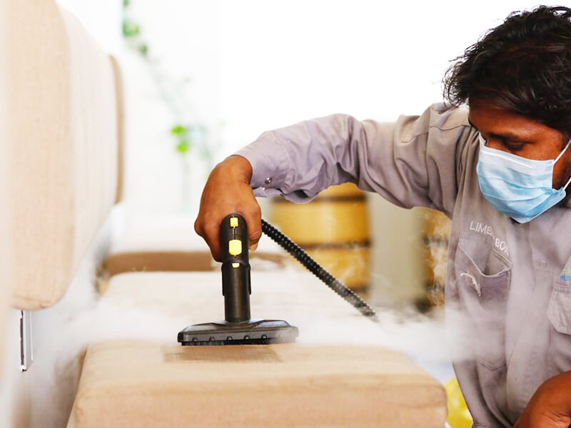 Professional cleaner using a steam machine to sanitize a sofa as part of Perfect Reflection's cleaning services in Muscat